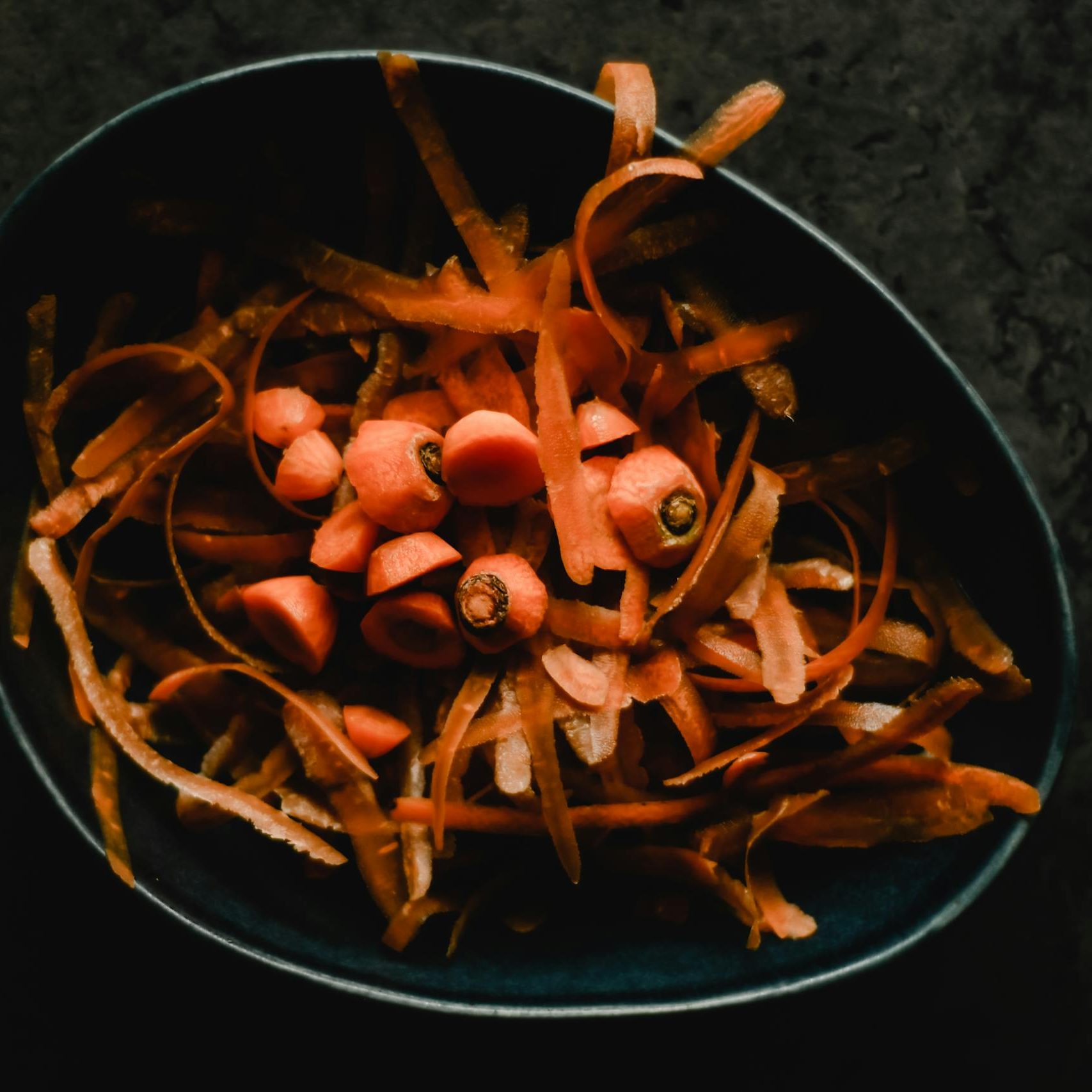 Carrot peels and scraps in a dark bowl.